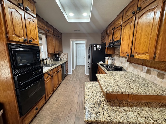 kitchen with visible vents, black appliances, a sink, under cabinet range hood, and backsplash