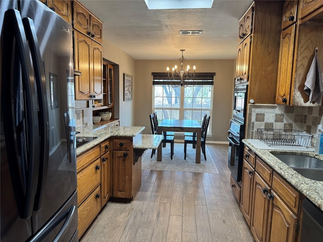 kitchen featuring light wood-type flooring, brown cabinets, black appliances, backsplash, and a chandelier