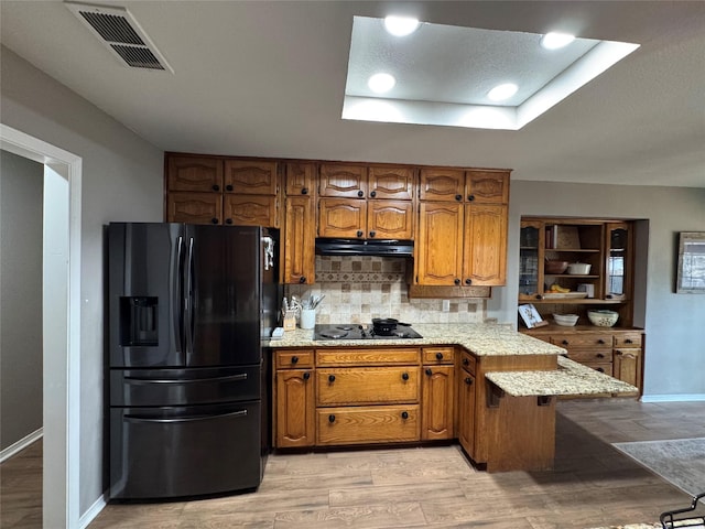 kitchen featuring visible vents, brown cabinets, black appliances, a peninsula, and exhaust hood