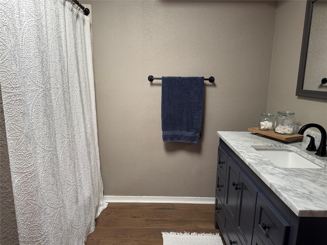 full bathroom with curtained shower, vanity, baseboards, and wood finished floors