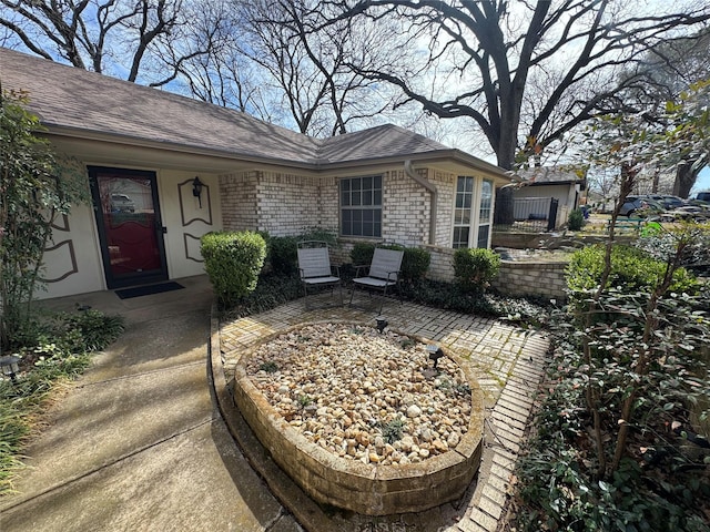 view of front of home featuring a patio area, brick siding, and roof with shingles