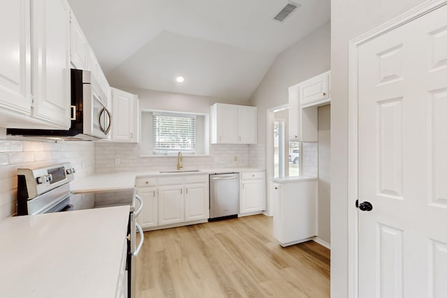 kitchen with visible vents, a sink, appliances with stainless steel finishes, white cabinets, and lofted ceiling