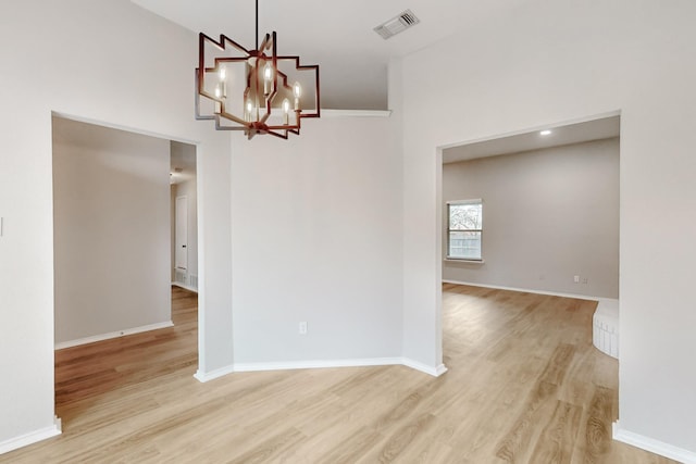 empty room featuring a chandelier, visible vents, baseboards, and light wood-style floors