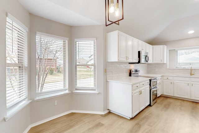 kitchen featuring a sink, light countertops, light wood-style floors, appliances with stainless steel finishes, and backsplash