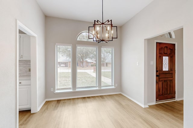 unfurnished dining area featuring light wood finished floors, baseboards, and an inviting chandelier