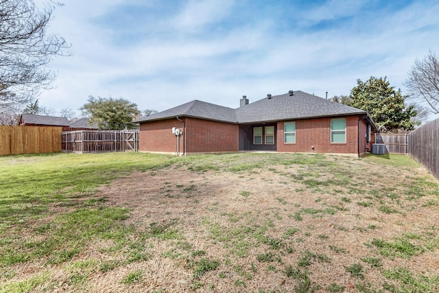 back of property with brick siding, a fenced backyard, a shingled roof, and a yard