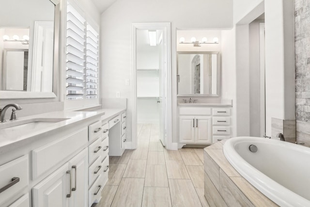 bathroom with a sink, lofted ceiling, two vanities, and a bath