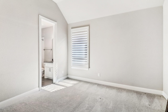 unfurnished bedroom featuring vaulted ceiling, multiple windows, light colored carpet, and baseboards