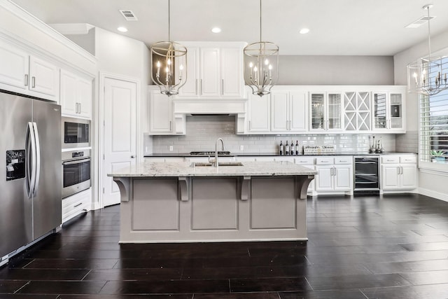 kitchen with tasteful backsplash, glass insert cabinets, appliances with stainless steel finishes, a notable chandelier, and a sink