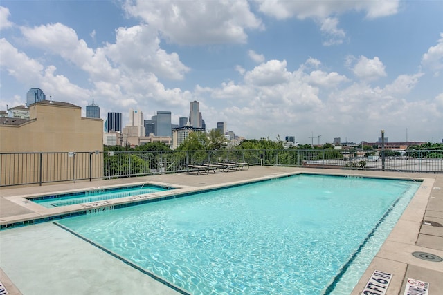 view of swimming pool featuring a city view, a hot tub, and fence