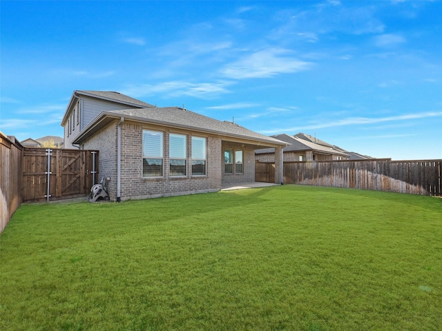 back of house featuring a gate, a fenced backyard, a yard, brick siding, and a patio area