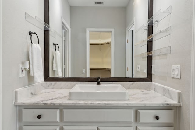 bathroom with visible vents, a walk in closet, and vanity