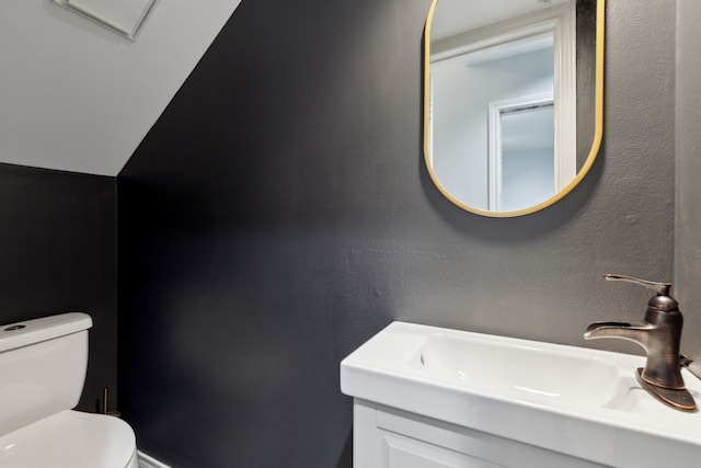 half bathroom featuring toilet, a textured wall, and a sink