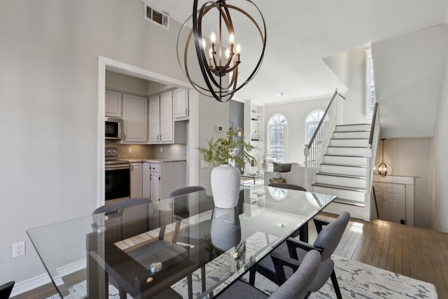 dining room featuring visible vents, hardwood / wood-style flooring, an inviting chandelier, baseboards, and stairs