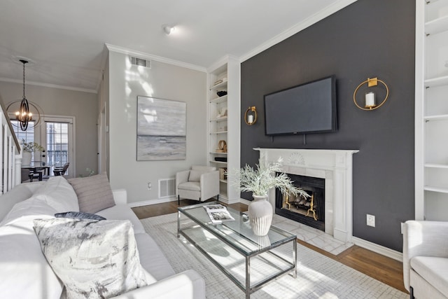 living room with visible vents, built in shelves, a notable chandelier, and wood finished floors