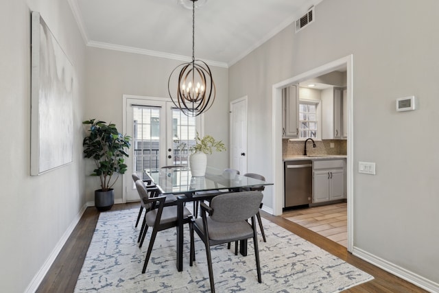 dining room featuring visible vents, ornamental molding, light wood-style flooring, baseboards, and a chandelier