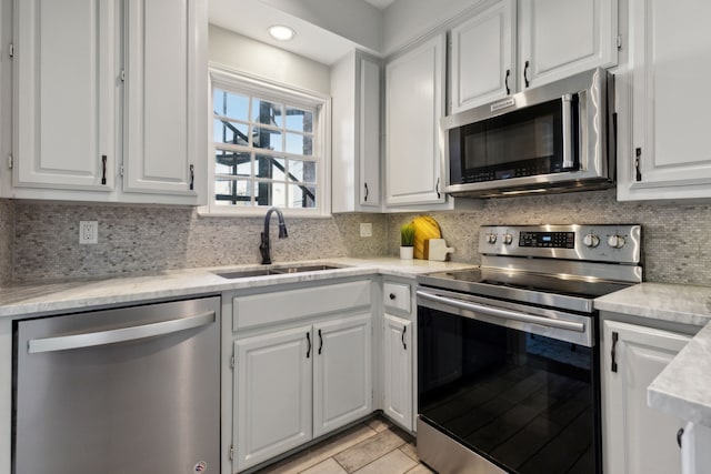 kitchen featuring backsplash, light countertops, appliances with stainless steel finishes, white cabinetry, and a sink