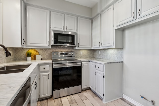 kitchen featuring appliances with stainless steel finishes, white cabinetry, light wood-type flooring, and a sink