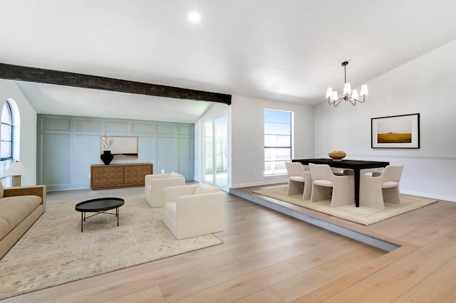 living room featuring a decorative wall, baseboards, lofted ceiling with beams, wood finished floors, and a notable chandelier