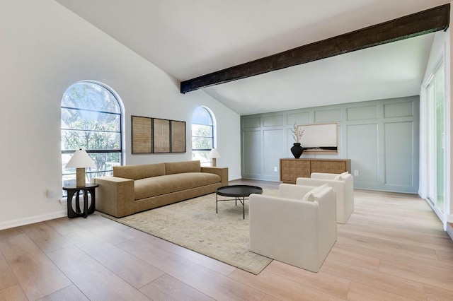 living area with light wood finished floors, a decorative wall, lofted ceiling with beams, and baseboards