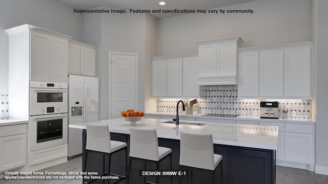 kitchen featuring white appliances, an island with sink, a sink, light countertops, and white cabinets