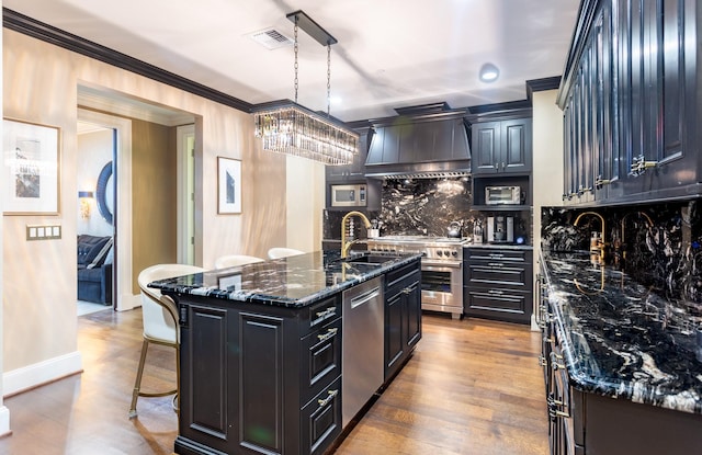 kitchen featuring visible vents, wall chimney range hood, ornamental molding, appliances with stainless steel finishes, and a kitchen breakfast bar