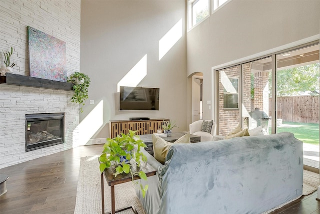 living area with arched walkways, a stone fireplace, a healthy amount of sunlight, and wood finished floors