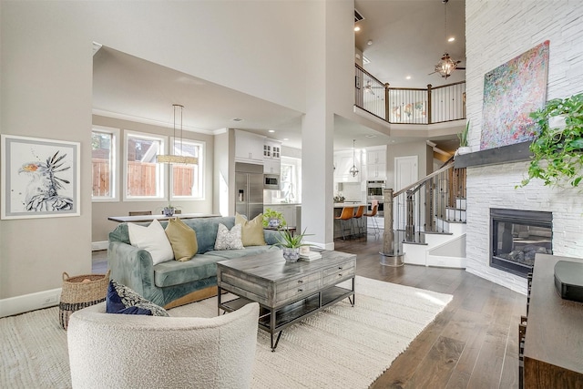 living room featuring stairway, wood-type flooring, a stone fireplace, crown molding, and baseboards