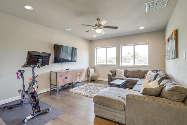 living room featuring wood finished floors, a ceiling fan, visible vents, and baseboards