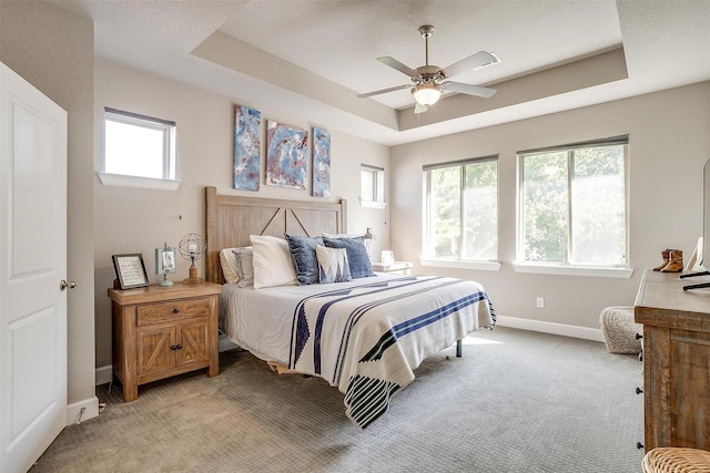 bedroom featuring ceiling fan, a tray ceiling, baseboards, and light carpet