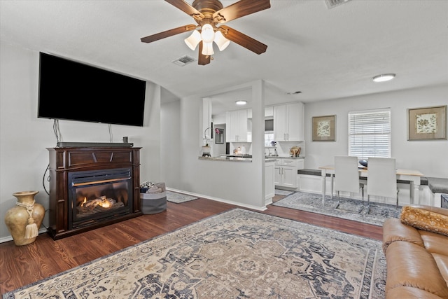 living area with visible vents, baseboards, a ceiling fan, and dark wood-style flooring