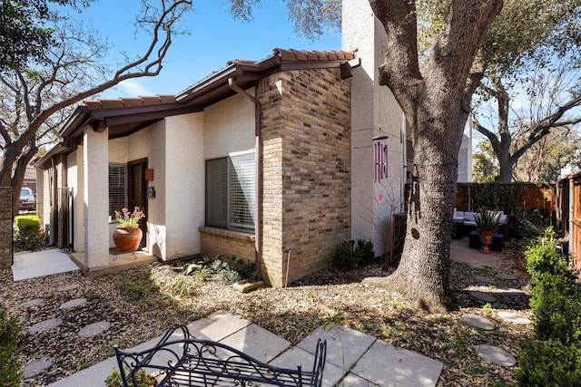 view of property exterior featuring a tiled roof, fence, brick siding, and a patio area