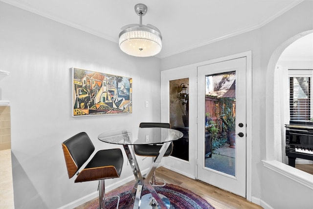 dining space with crown molding, wood finished floors, arched walkways, and baseboards