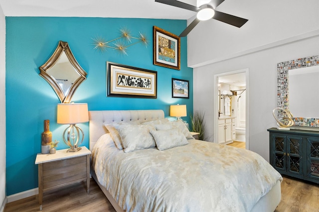 bedroom featuring vaulted ceiling, ensuite bath, baseboards, and wood finished floors