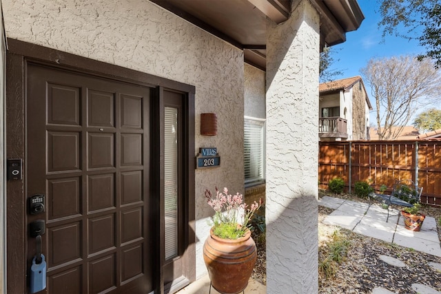 doorway to property with stucco siding and fence