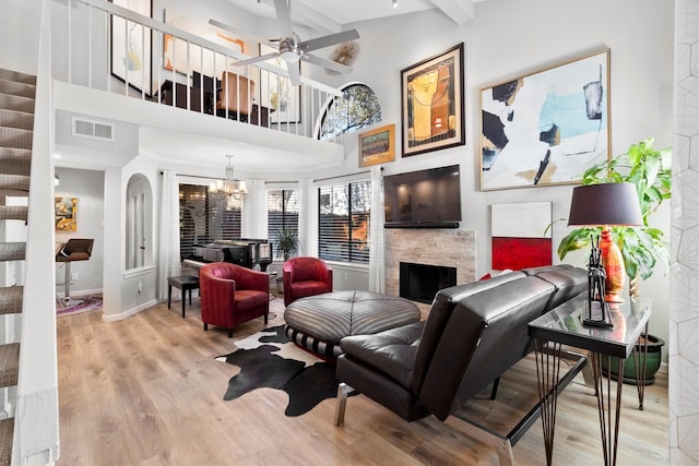 living area featuring visible vents, baseboards, light wood-style flooring, a fireplace, and ceiling fan with notable chandelier