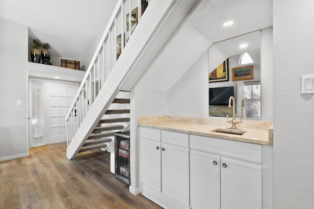 bar featuring wood finished floors, lofted ceiling, a sink, stairs, and a textured wall