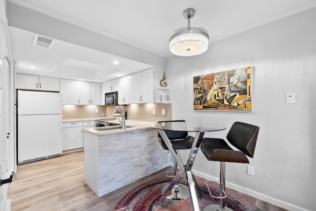 kitchen with visible vents, tasteful backsplash, freestanding refrigerator, a peninsula, and black microwave