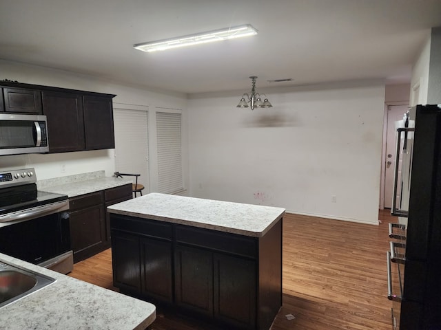 kitchen with visible vents, a kitchen island, wood finished floors, stainless steel appliances, and light countertops