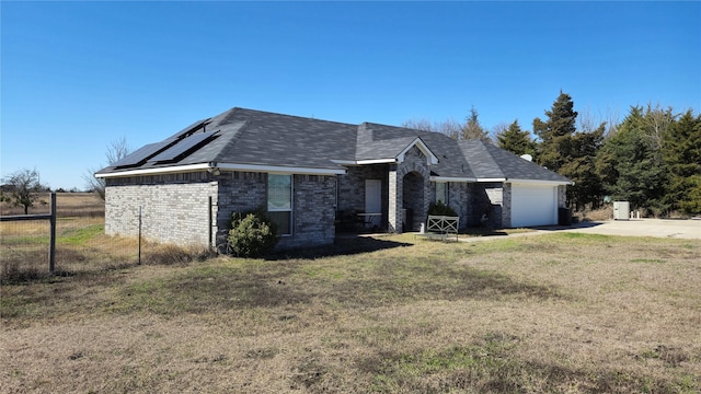 ranch-style home with a front yard, solar panels, an attached garage, concrete driveway, and brick siding