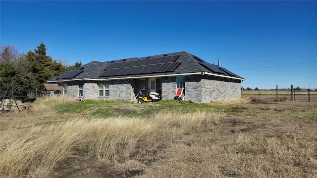 rear view of property with roof mounted solar panels, brick siding, and fence