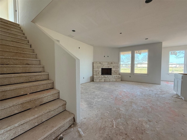 unfurnished living room with stairs and a stone fireplace