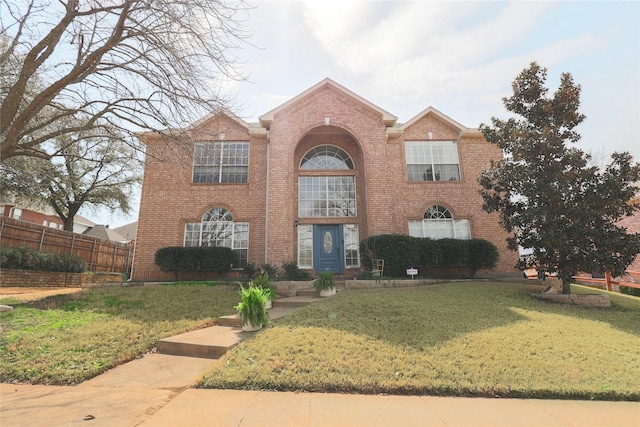 view of front of house with brick siding, a front yard, and fence