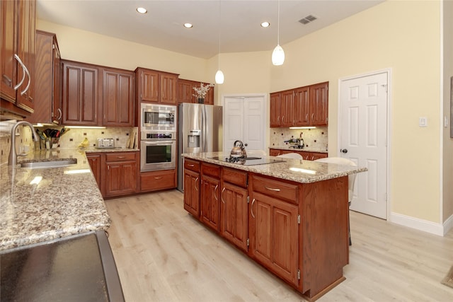 kitchen with visible vents, a kitchen island, light wood-style flooring, a sink, and appliances with stainless steel finishes