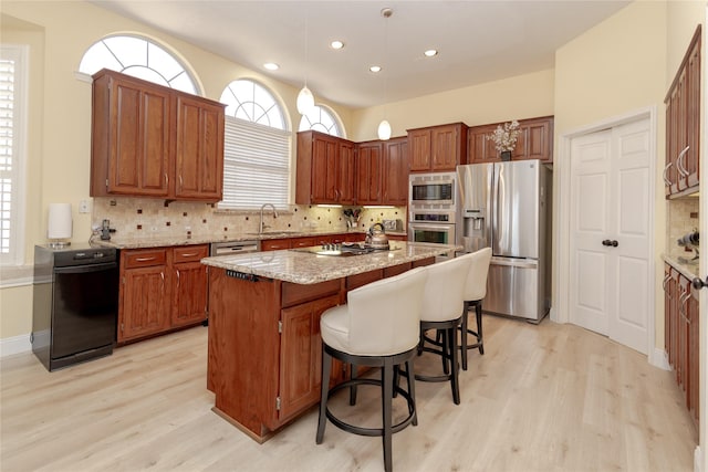 kitchen featuring backsplash, a kitchen island, light stone countertops, stainless steel appliances, and a sink