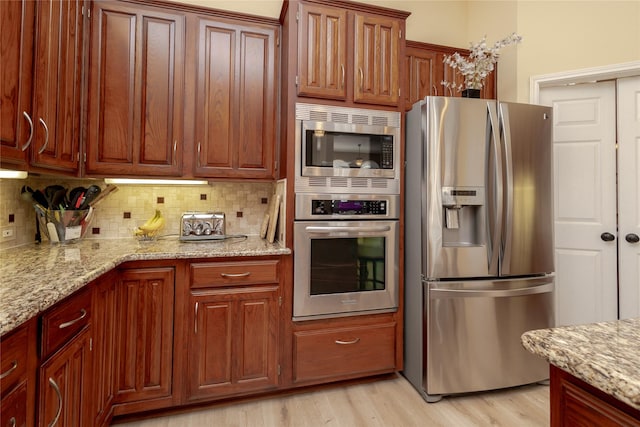 kitchen featuring decorative backsplash, light wood-style flooring, light stone counters, and appliances with stainless steel finishes