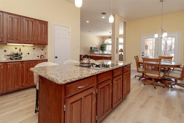 kitchen with light wood-type flooring, a kitchen island, backsplash, and hanging light fixtures