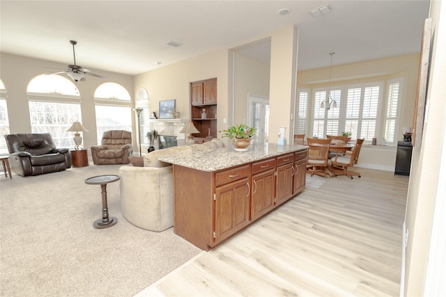 kitchen with light stone countertops, visible vents, ceiling fan, light wood-style floors, and open floor plan