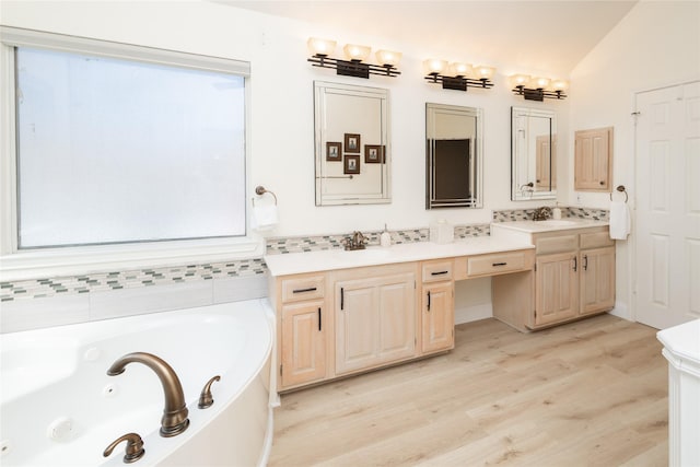 full bath with vanity, wood finished floors, a tub with jets, lofted ceiling, and decorative backsplash