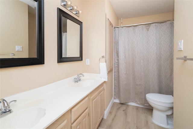 bathroom featuring double vanity, wood finished floors, toilet, and a sink